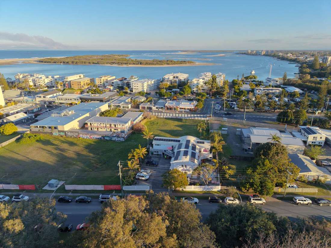Aerial view of CALI Backpackers with Pumicestone Passage and the ocean behind at golden hour