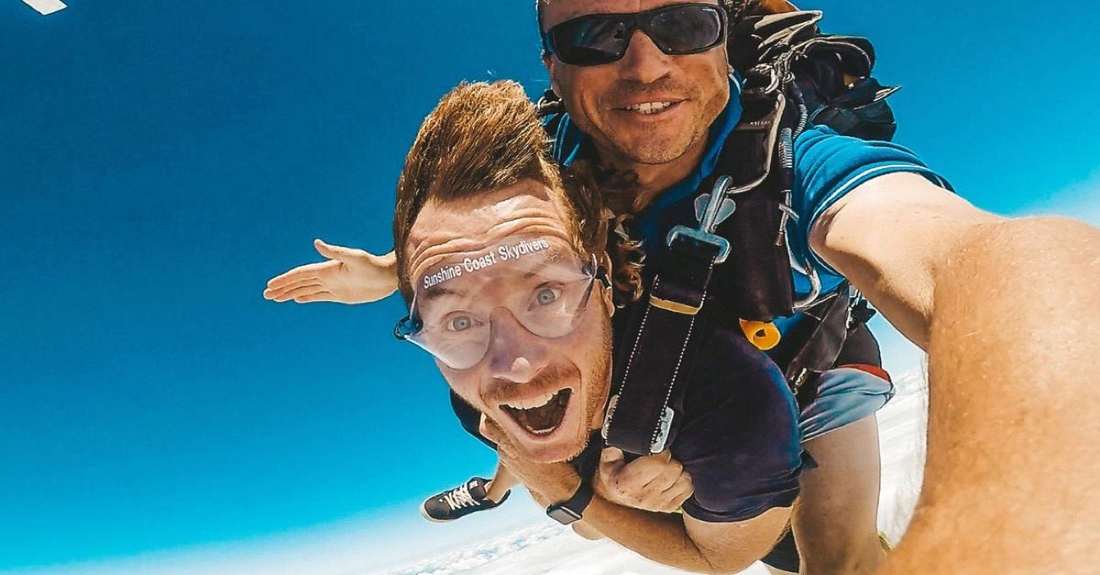 A grinning tandem skydiver in freefall over the Sunshine Coast
